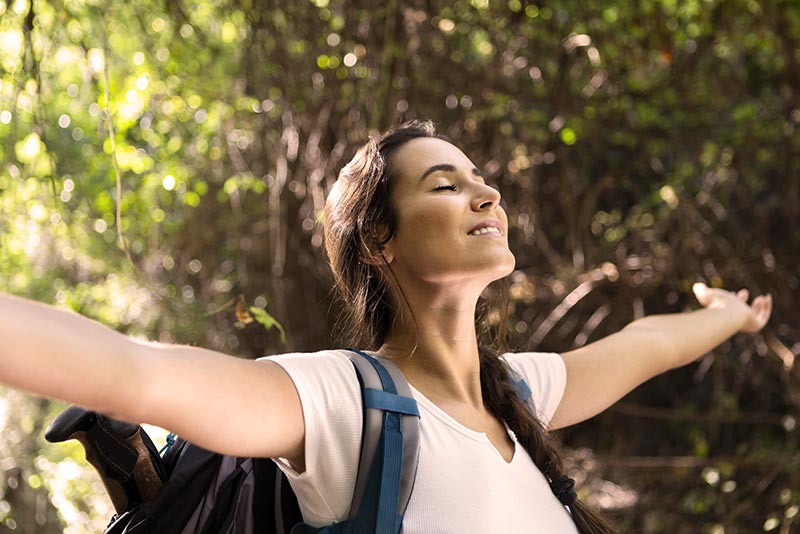 Femme épanouie et en harmonie avec la nature, les yeux fermés et les bras ouverts