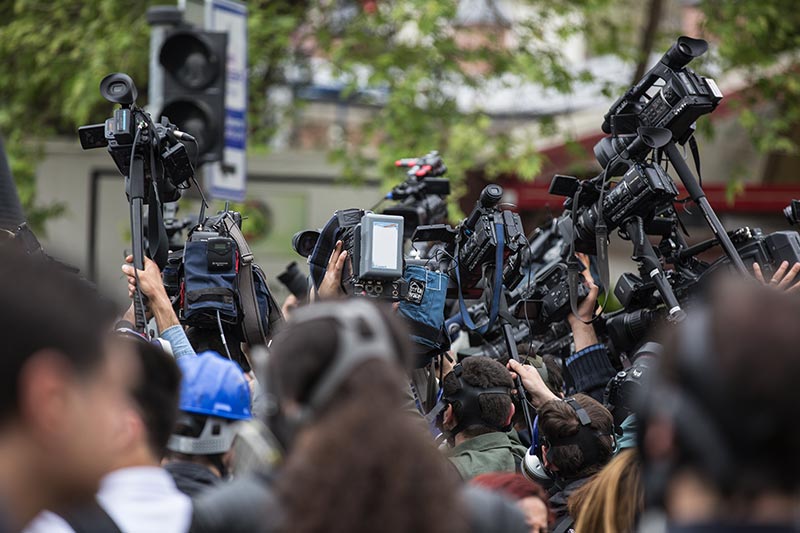Une foule de journalistes, avec micros et caméras, couvre l'événement où Simone Biles annonce sa décision de se retirer de certaines épreuves aux Jeux Olympiques de Tokyo 2020 pour des raisons de santé mentale. Cette couverture médiatique intense reflète l'impact mondial de son choix audacieux.