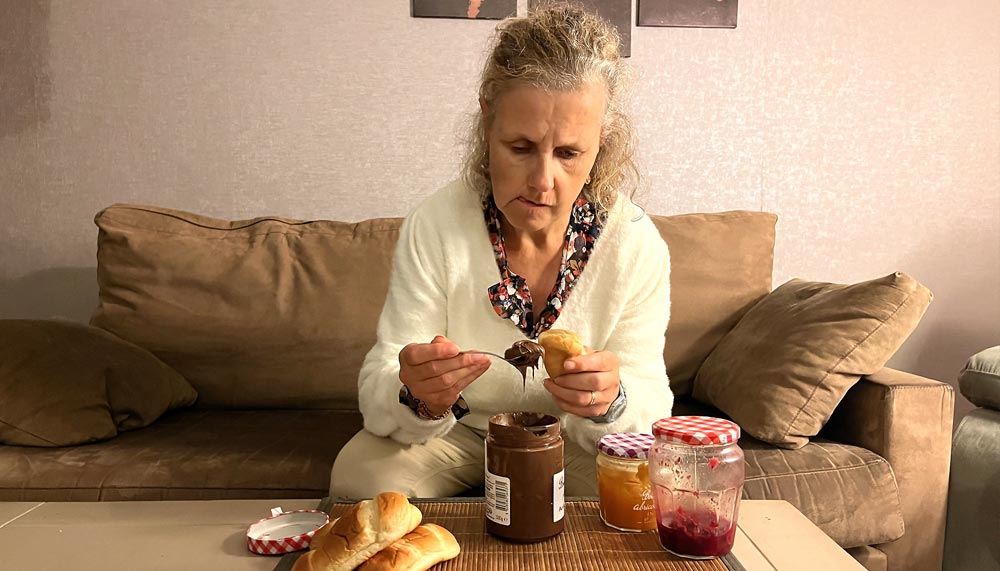 Béa, fondatrice de Femmes en Harmonie, regarde d’un air agacé un pain au lait tartiné de chocolat, symbolisant la difficulté d’arrêter de manger ses émotions face au stress et aux blessures émotionnelles. Te reconnais-tu dans cette habitude de chercher du réconfort dans la nourriture ?