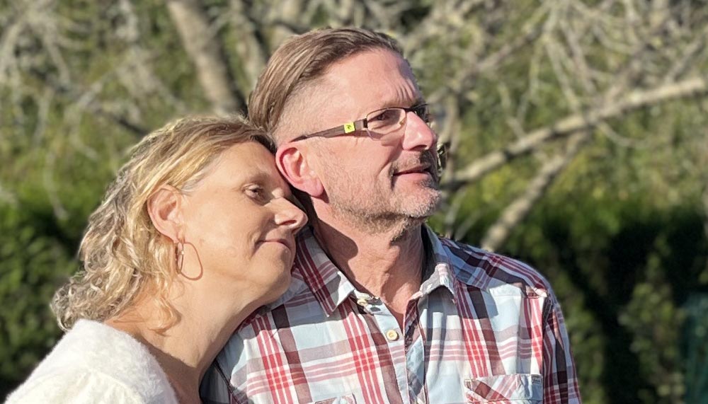 Gros plan sur Béa posant tendrement sa tête sur l'épaule de Vincent, son mari, regardant ensemble l’horizon dans leur jardin, symbolisant la complicité et l’importance de booster sa libido pour une vie intime épanouie après 45 ans.
