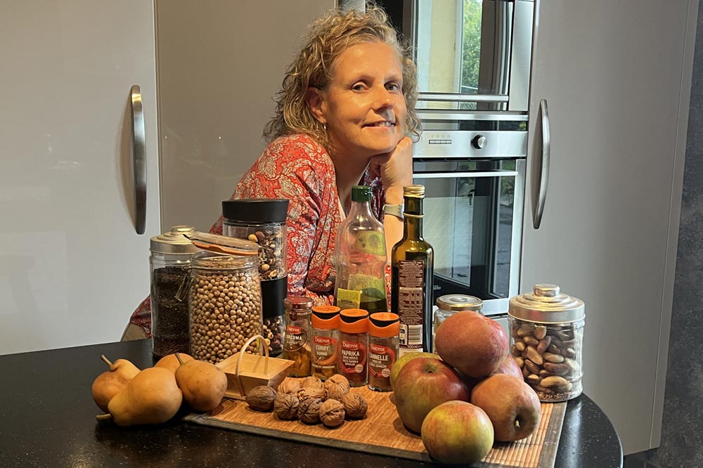 Béa, créatrice de Femmes en Harmonie, se tient dans sa cuisine entourée d'ingrédients sains et nutritifs, illustrant l'importance de cuisiner des plats réconfortants. Cette image souligne l'utilisation de produits frais et de qualité pour préparer des repas équilibrés et savoureux.