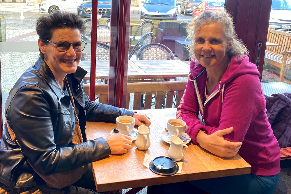 Sandra et Béa, la créatrice de Femmes en Harmonie, échangeant dans un café et symbolisant l'importance de la solidarité et du partage d'expériences face au syndrome du nid vide et aux épreuves émotionnelles.