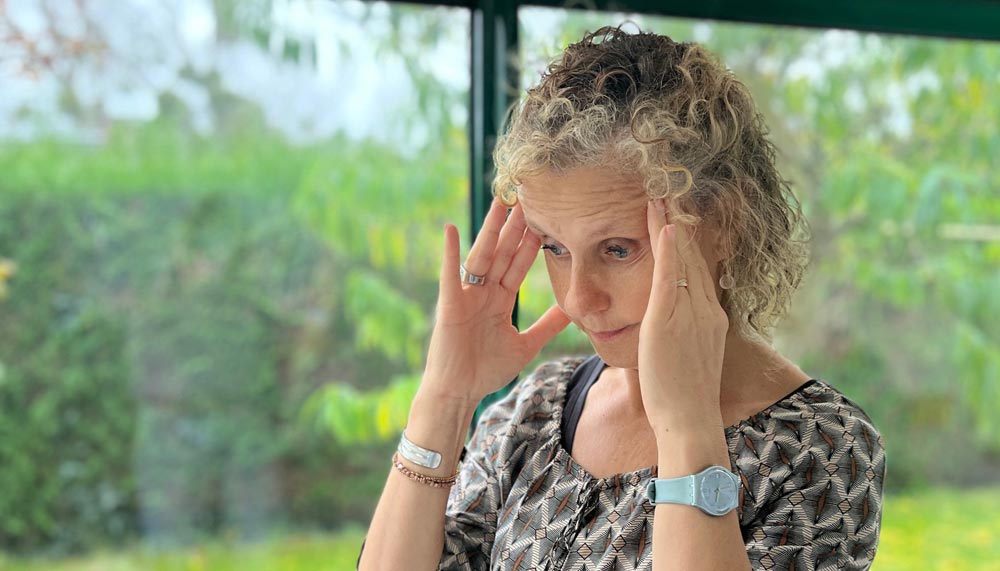 Béa, la fondatrice de Femmes en Harmonie, se tient la tête dans les mains, exprimant une réflexion intense. Cette image illustre les moments où les pensées deviennent envahissantes et montrent la nécessité de découvrir comment arrêter de trop penser. L’article propose quatre clés efficaces pour apaiser le mental et alléger l’esprit.