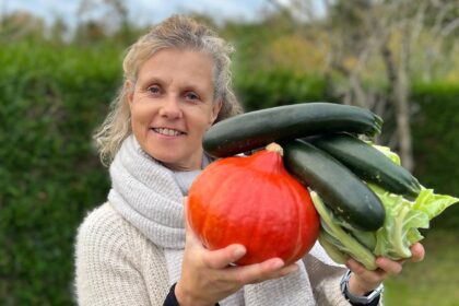 Béa, fondatrice de Femmes en Harmonie, tenant des légumes frais : potimarron, courgettes et chou vert, dans son jardin. Une illustration inspirante des bienfaits de manger des légumes pour une alimentation saine et équilibrée.