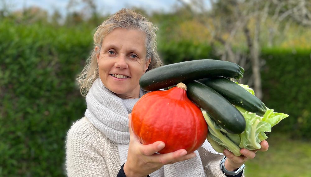 Béa, fondatrice de Femmes en Harmonie, tenant des légumes frais : potimarron, courgettes et chou vert, dans son jardin. Une illustration inspirante des bienfaits de manger des légumes pour une alimentation saine et équilibrée.