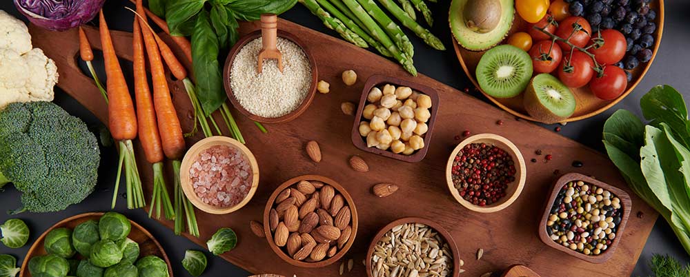 Assortiment coloré d’aliments riches en fibres alimentaires sur une table en bois : légumes frais, fruits entiers, graines, légumineuses et céréales complètes, sources naturelles de fibres pour améliorer la digestion, la satiété et le transit après 50 ans.