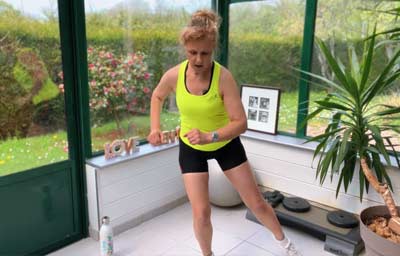 Béa réalise un exercice de fente latérale avec jambe arrière dans une véranda lumineuse. Ce mouvement fait partie des exercices pour brûler les graisses à la maison, conçus pour tonifier les cuisses, les fessiers et les abdominaux, relancer le métabolisme et favoriser une remise en forme douce et efficace après 50 ans.