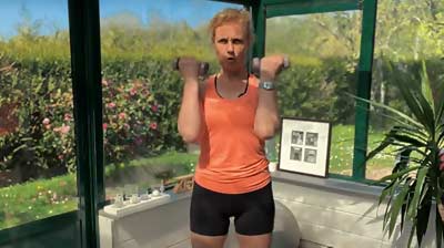 Béa effectue le premier exercice de la séance d'exercices de musculation douce pour femmes après 50 ans : debout, haltères en prise supination, gainage actif, pour tonifier les biceps et la sangle abdominale en douceur.