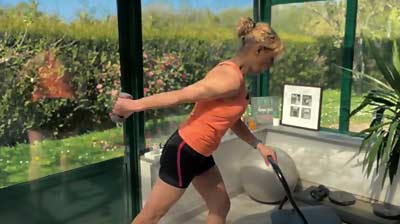 Béa montre le 3ème exercice de la séance de musculation douce en appui sur une chaise, coude collé au corps, bras tendu vers l’arrière avec un haltère léger pour renforcer les triceps en toute sécurité.