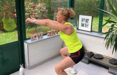 Béa exécute un squat avec montée des bras dans sa véranda lumineuse. Ce mouvement fait partie des exercices les plus efficaces pour engager l’ensemble du corps et perdre du poids. Il renforce les jambes, les fessiers, les abdos et les épaules, améliore la posture, stimule la combustion des calories et contribue à une silhouette tonique et équilibrée.