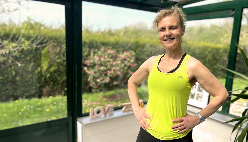 Béa, fondatrice de Femmes en Harmonie, en tenue de sport dans sa véranda, prête à guider sur des exercices pour brûler les graisses. Cette séance te permettra de tonifier ton corps, relancer ton métabolisme et retrouver de l’énergie après 50 ans.